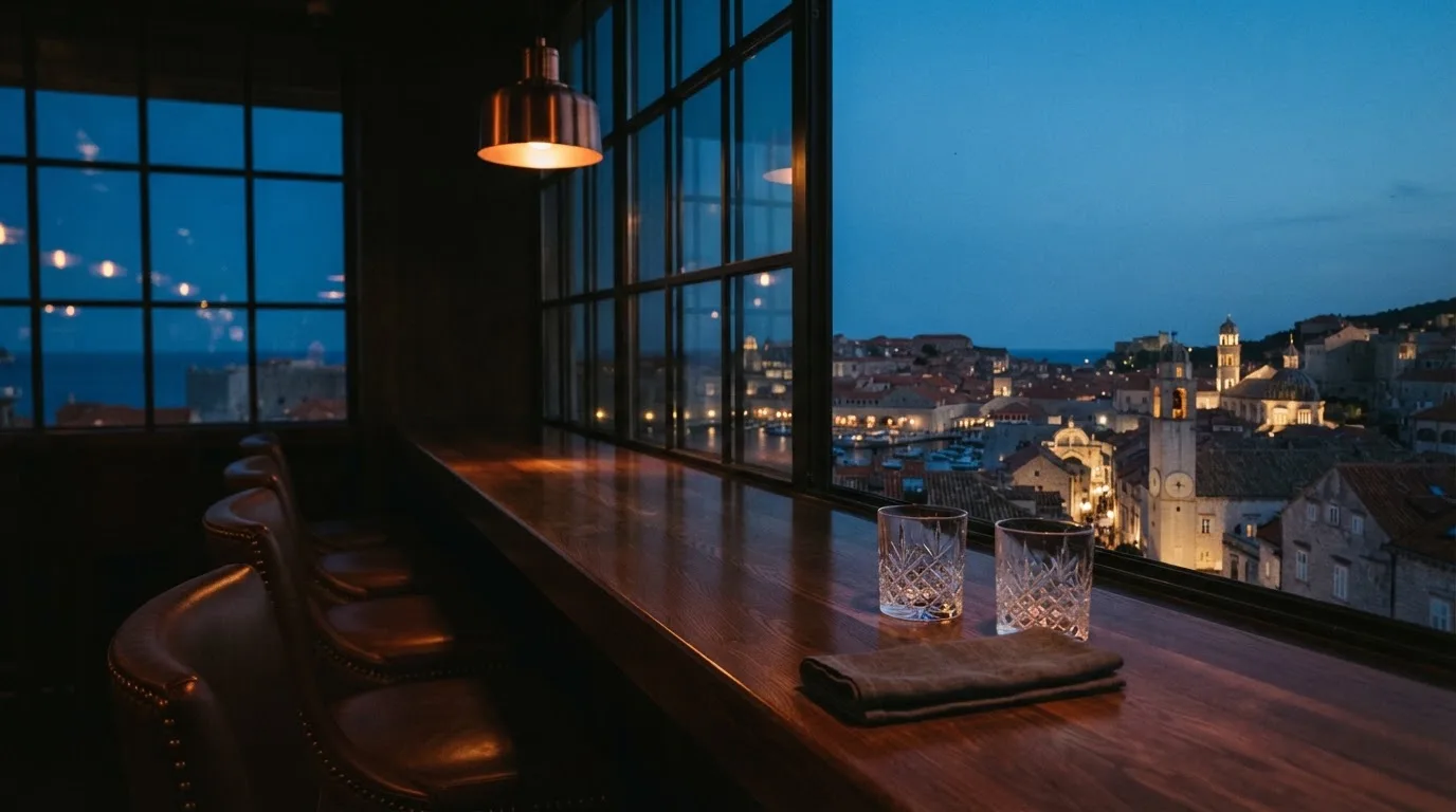 Pogled kroz prozor casina na večernji grad, bar s čašama i praznim stolicama, topla svjetla.