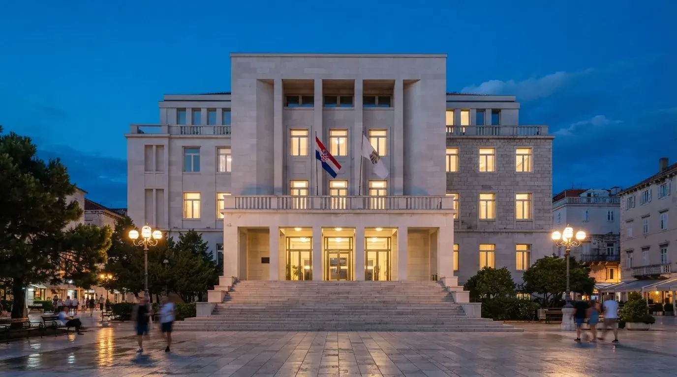 Moderna zgrada s kamenim pročeljem i velikim ulaznim stubama u središtu grada, snimljena u sumrak.